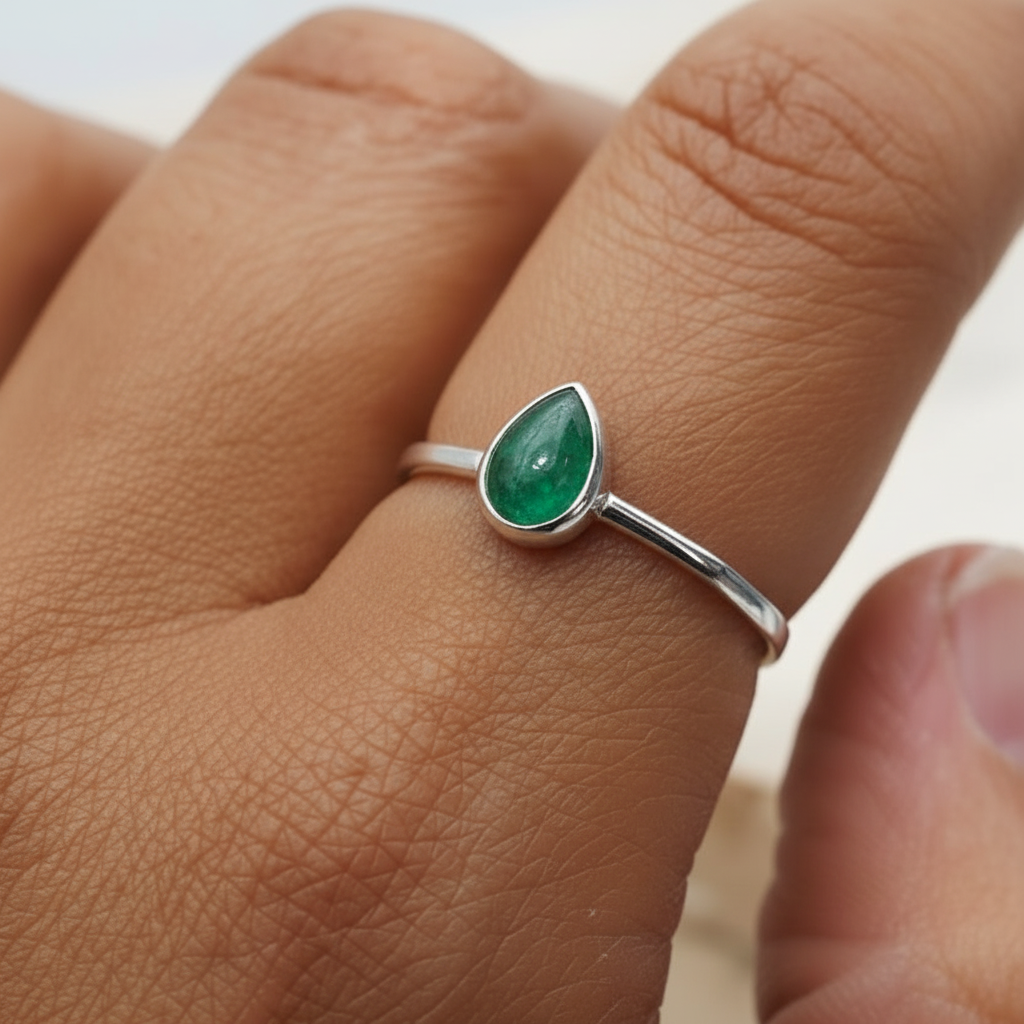 sterling Silver ring with a green emerald gemstone on a person's finger against a neutral background