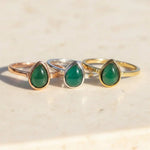 Three rings in rose gold, silver and gold with may birthstone emerald teardrop gemstones on a wooden surface