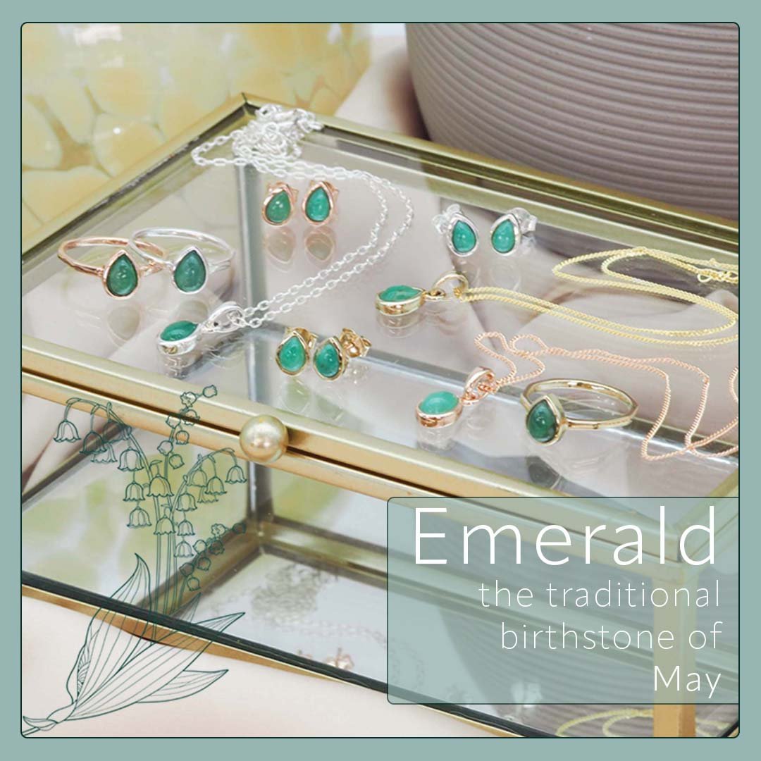 May Birthstone Jewellery set with emerald stones on a glass surface, featuring text about emeralds as the traditional birthstone of May.
