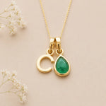 Gold May birthstone necklace with a pear-shaped natural emerald gemstone pendant and letter 'C' charm on a light background.