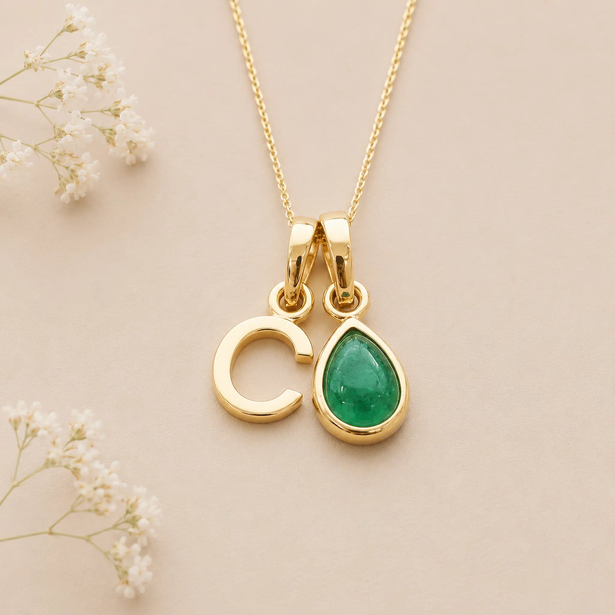 Gold May birthstone necklace with a pear-shaped natural emerald gemstone pendant and letter 'C' charm on a light background.