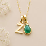 Gold necklace with 'Z' letter pendant and may birthstone emerald teardrop charm on a beige background