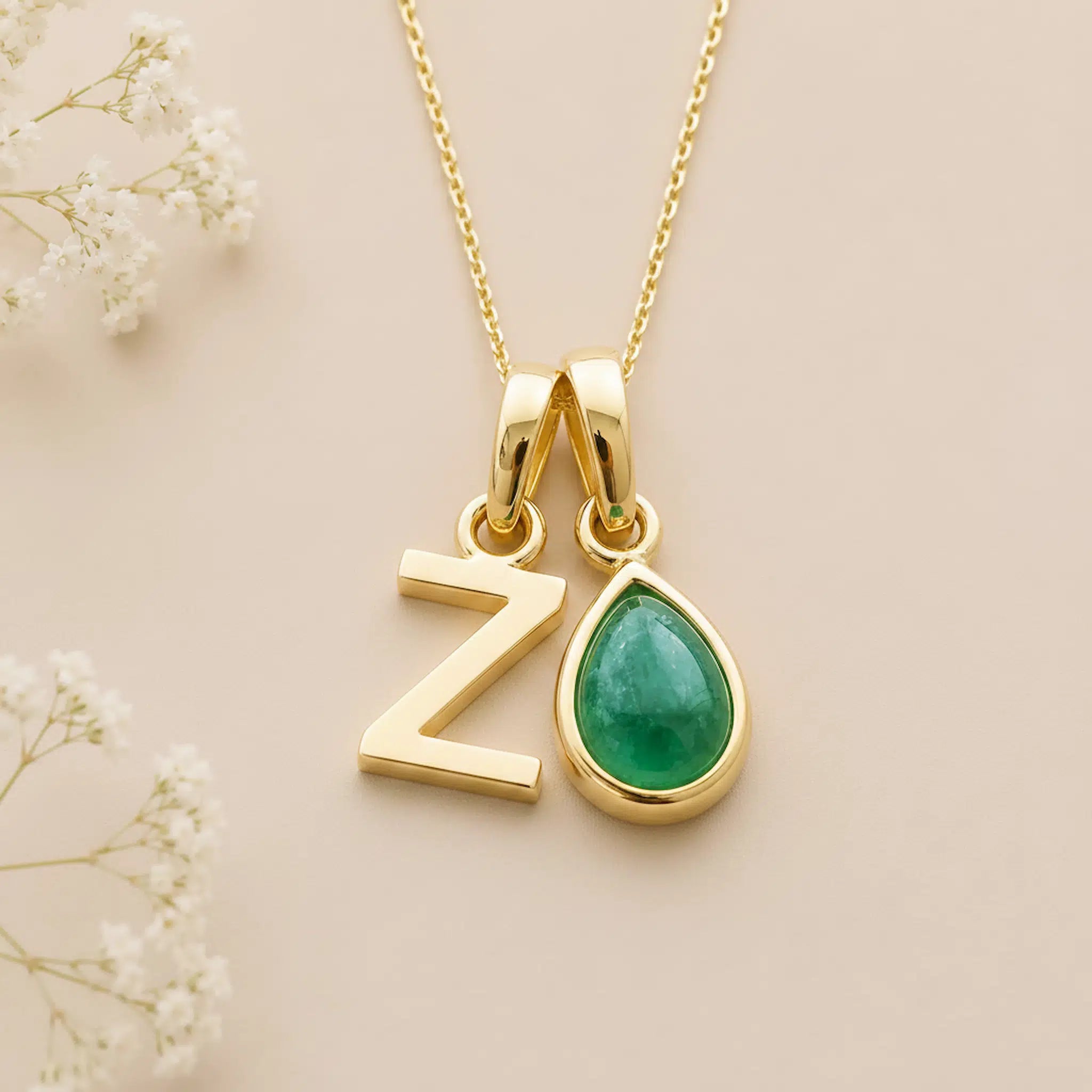 Gold necklace with 'Z' letter pendant and may birthstone emerald teardrop charm on a beige background