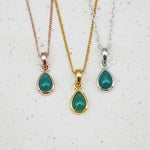 Three may birthstone necklaces with teardrop-shaped natural emerald gemstone pendants on gold, rose gold, and silver chains against a light background.