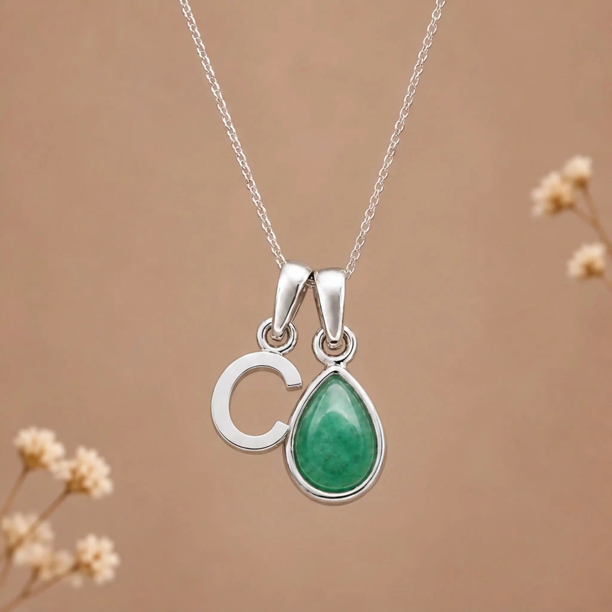 sterling silver initial c may birthstone natural emerald pendant necklace against a dark warm beige background