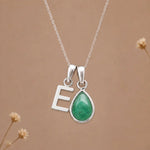 sterling silver initial e may birthstone natural emerald pendant necklace against a dark warm beige background