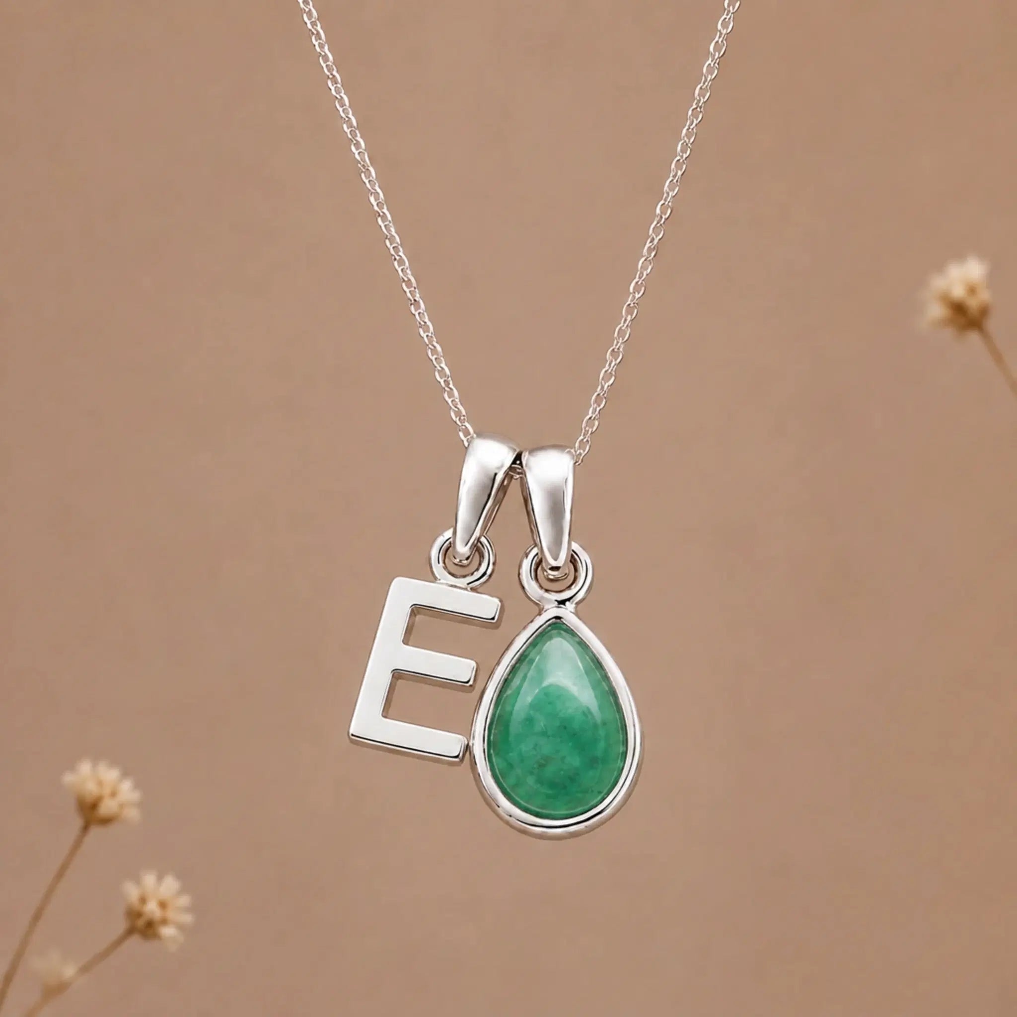 sterling silver initial e may birthstone natural emerald pendant necklace against a dark warm beige background