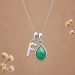 sterling silver initial f may birthstone natural emerald pendant necklace against a dark warm beige background