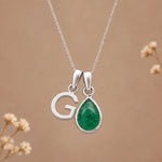 sterling silver initial g may birthstone natural emerald pendant necklace against a dark warm beige background