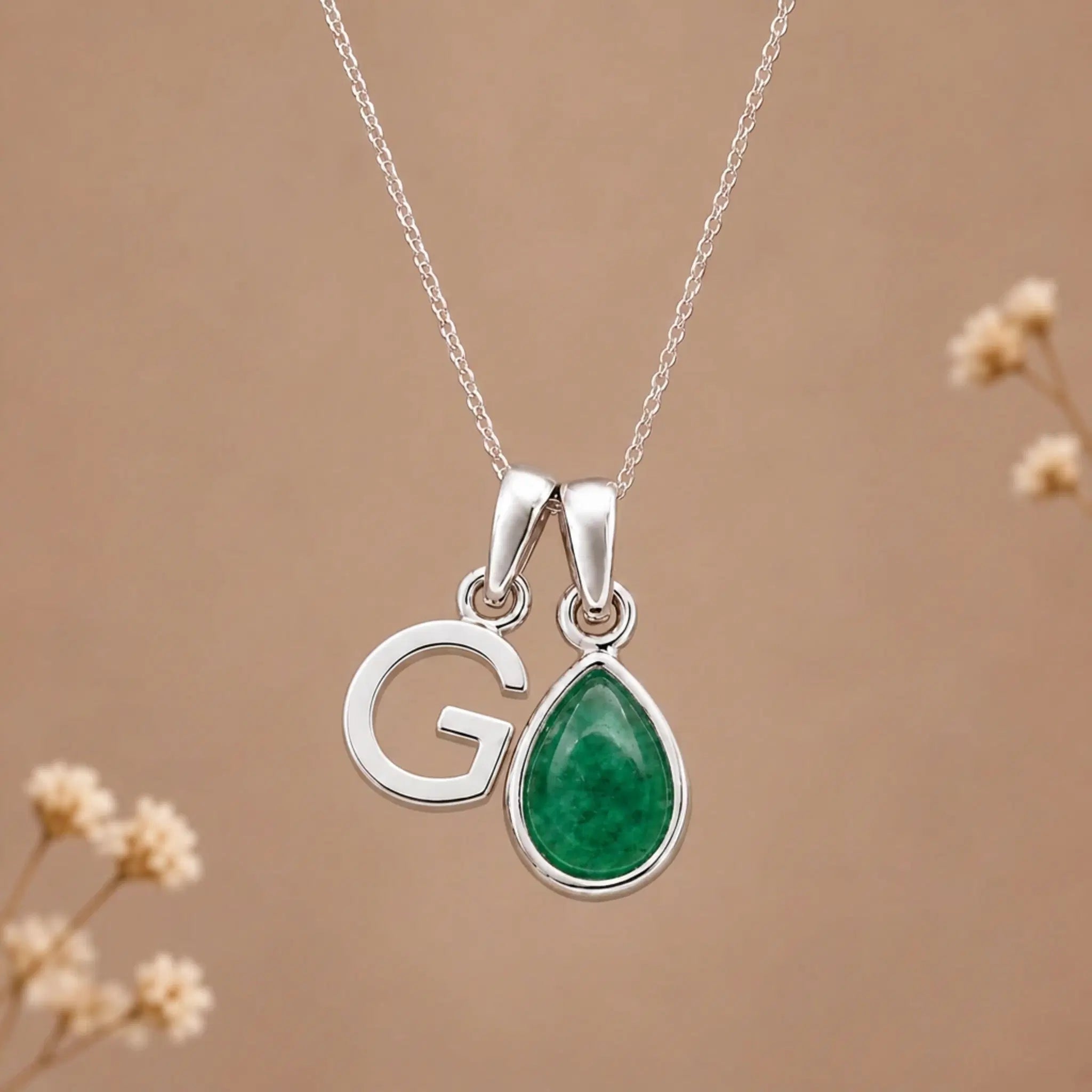 sterling silver initial g may birthstone natural emerald pendant necklace against a dark warm beige background