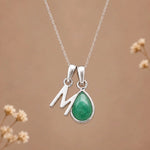 sterling silver initial m may birthstone natural emerald pendant necklace against a dark warm beige background