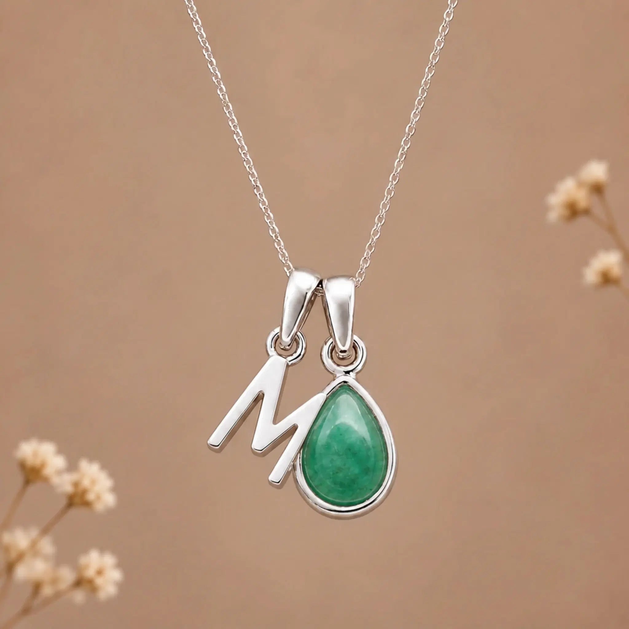 sterling silver initial m may birthstone natural emerald pendant necklace against a dark warm beige background