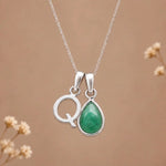 sterling silver initial q may birthstone natural emerald pendant necklace against a dark warm beige background