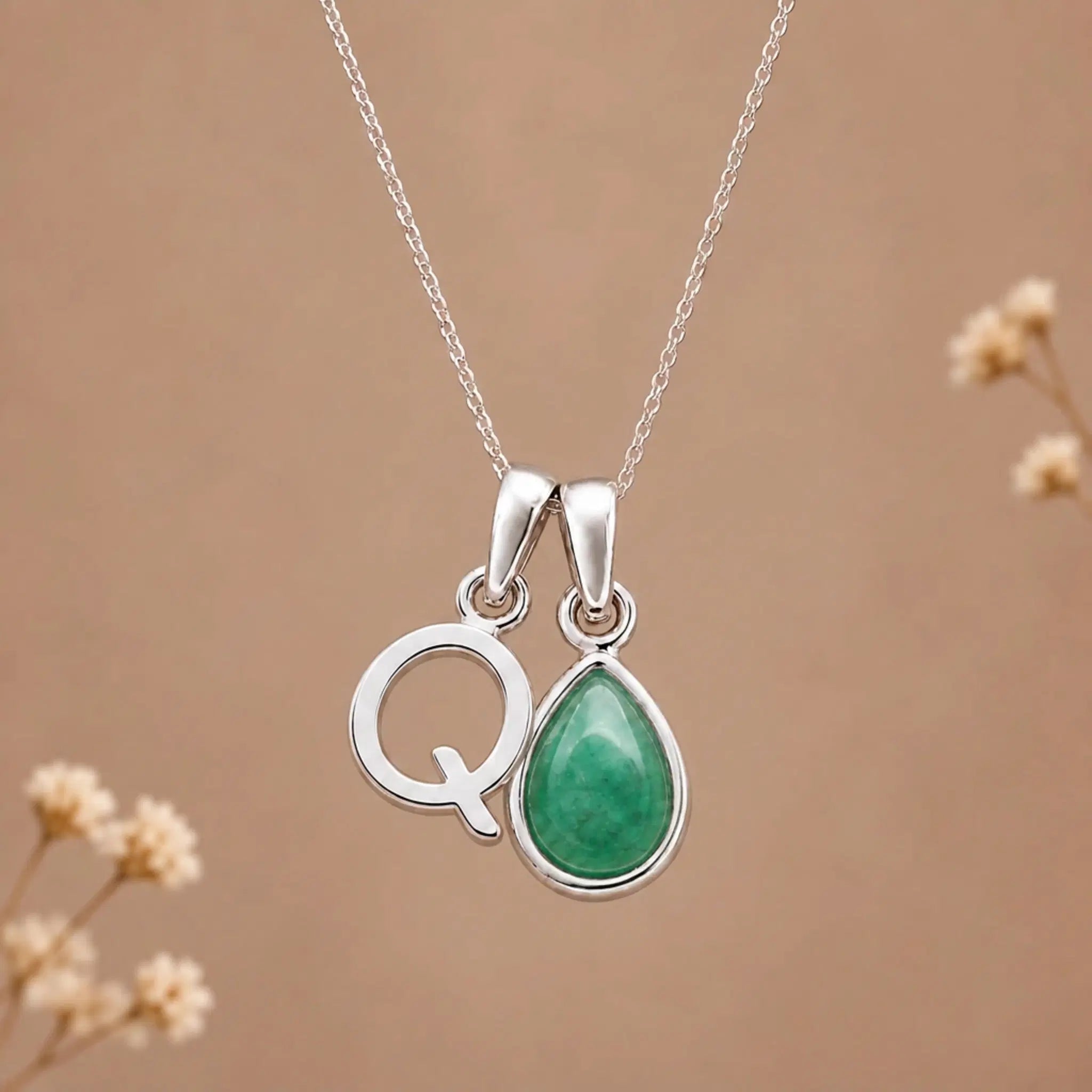 sterling silver initial q may birthstone natural emerald pendant necklace against a dark warm beige background