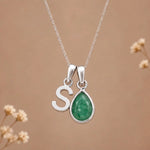 sterling silver initial s may birthstone natural emerald pendant necklace against a dark warm beige background