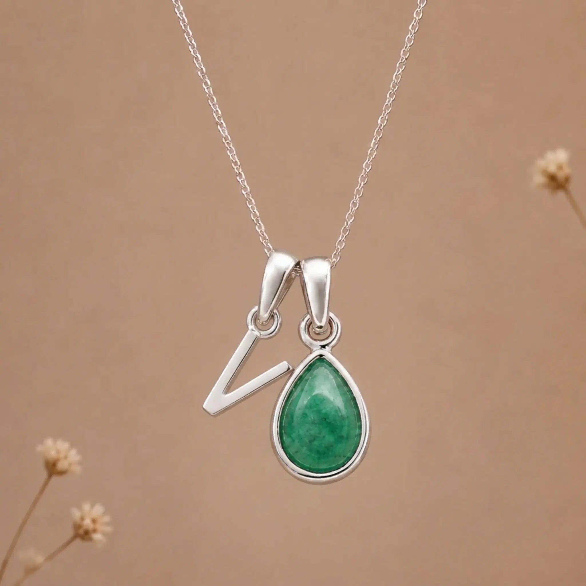 sterling silver initial v may birthstone natural emerald pendant necklace against a dark warm beige background