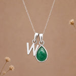 sterling silver initial w may birthstone natural emerald pendant necklace against a dark warm beige background