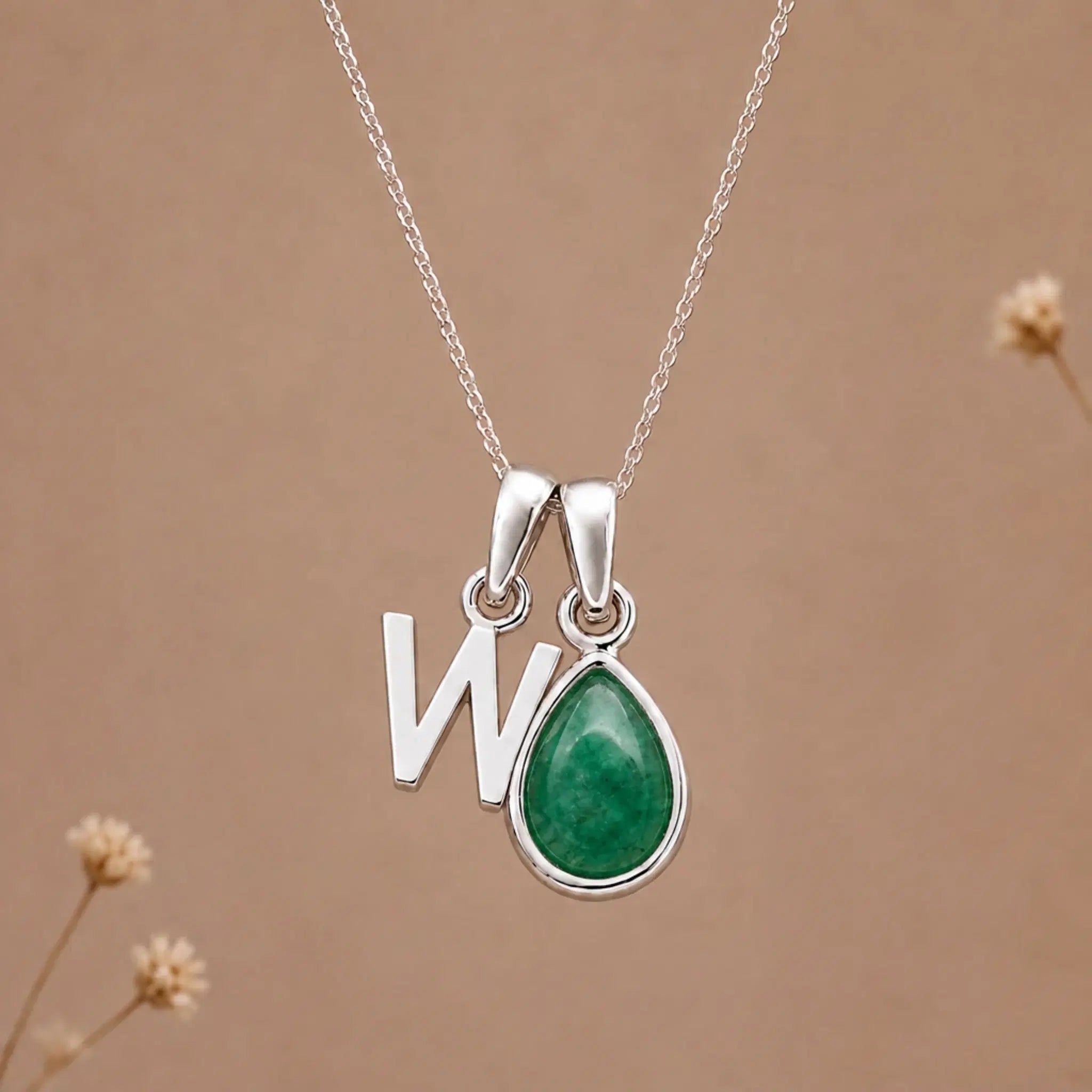 sterling silver initial w may birthstone natural emerald pendant necklace against a dark warm beige background