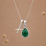 sterling silver initial x may birthstone natural emerald pendant necklace against a dark warm beige background