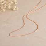 Minimalist 18k Rose Gold Curb Chain Necklace laying on a white stone surface