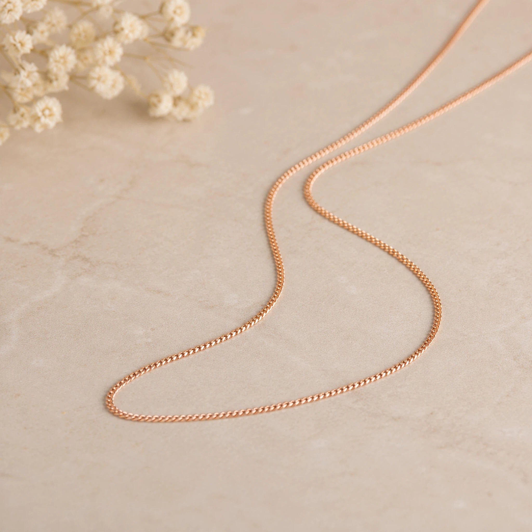 Minimalist 18k Rose Gold Curb Chain Necklace laying on a white stone surface