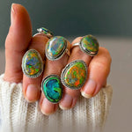 Monarch Opal Rings in different colourways worn across the fingers with a cream knit sleeve, close-up