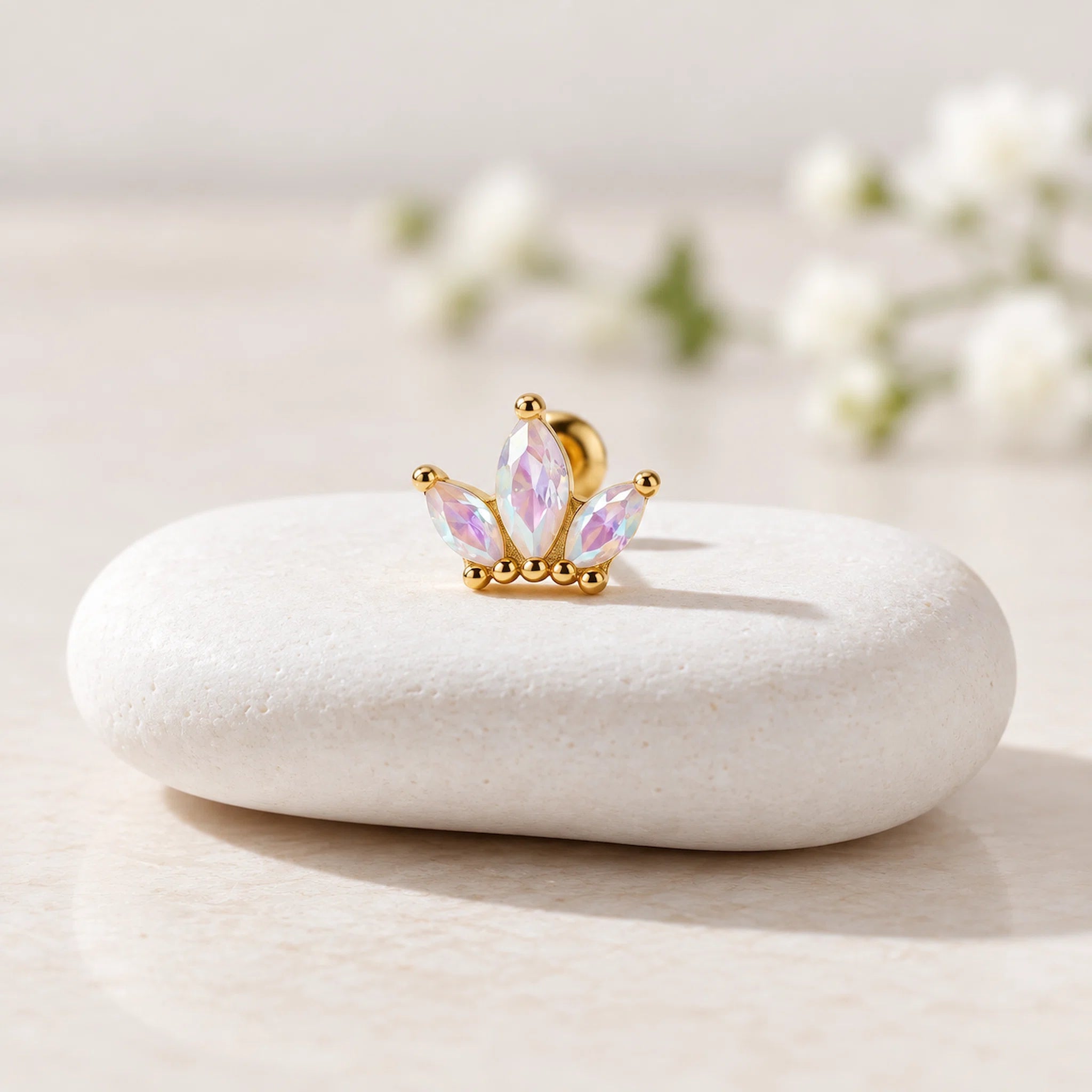 Gold and pink crown-shaped earring on a white stone surface