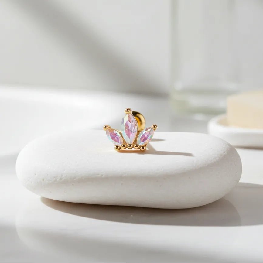 Gold and pink crown-shaped earring on a white stone surface