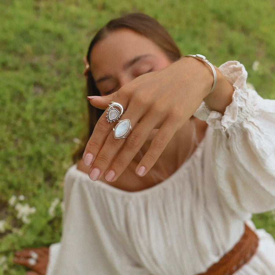 Woman in a field showing her hand to the camera, wearing two moonstone rings.