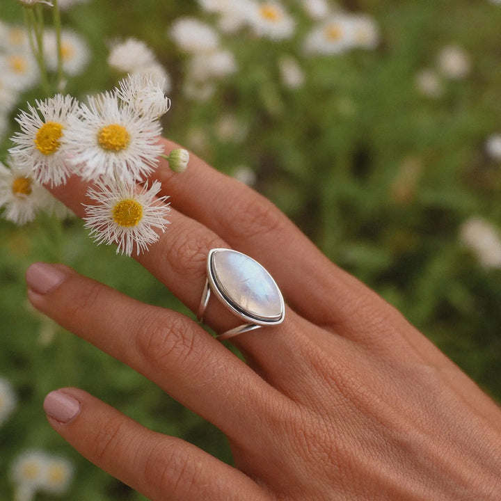 Woman's hand holding flowers and wearing a large moonstone ring.