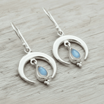 Silver moon-shaped earrings with teardrop moonstones on a wooden surface