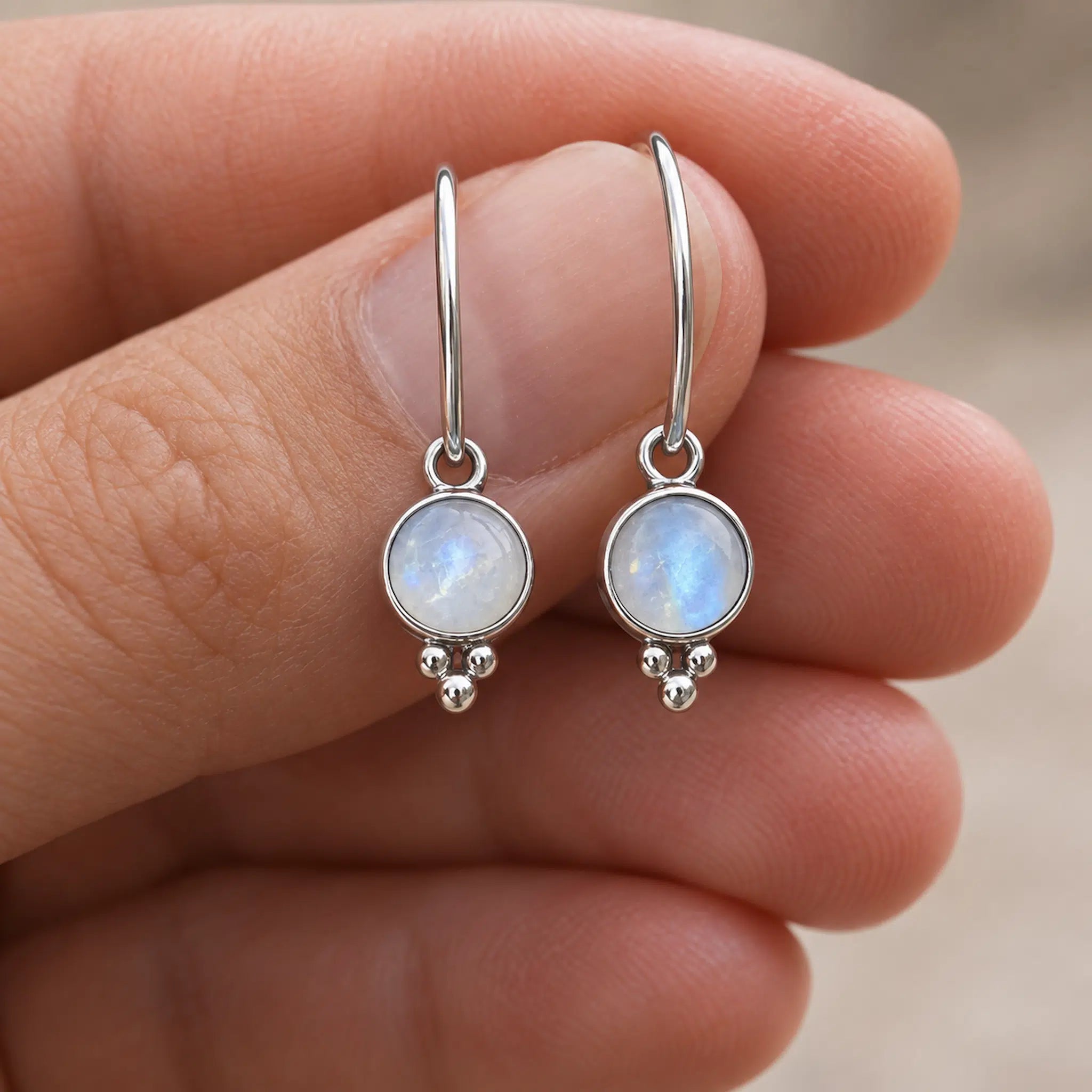 Silver moonstone hoop earrings held between fingers against a neutral background
