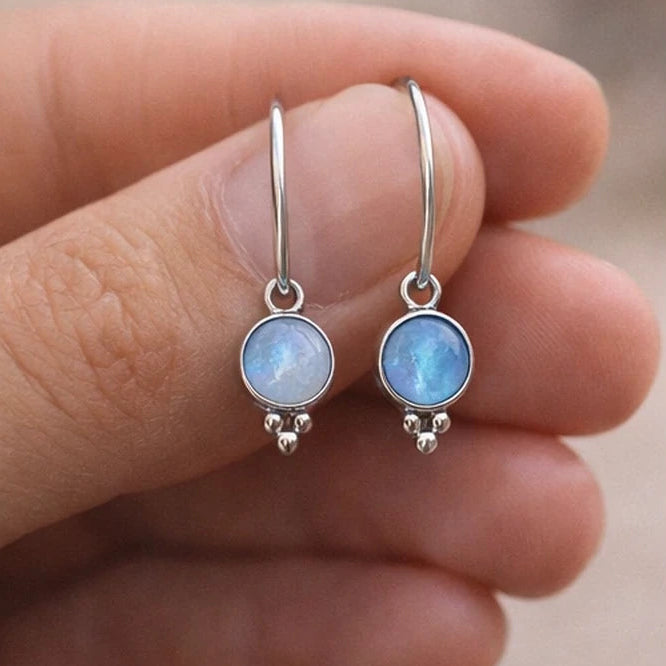 Silver moonstone hoop earrings held between fingers against a neutral background