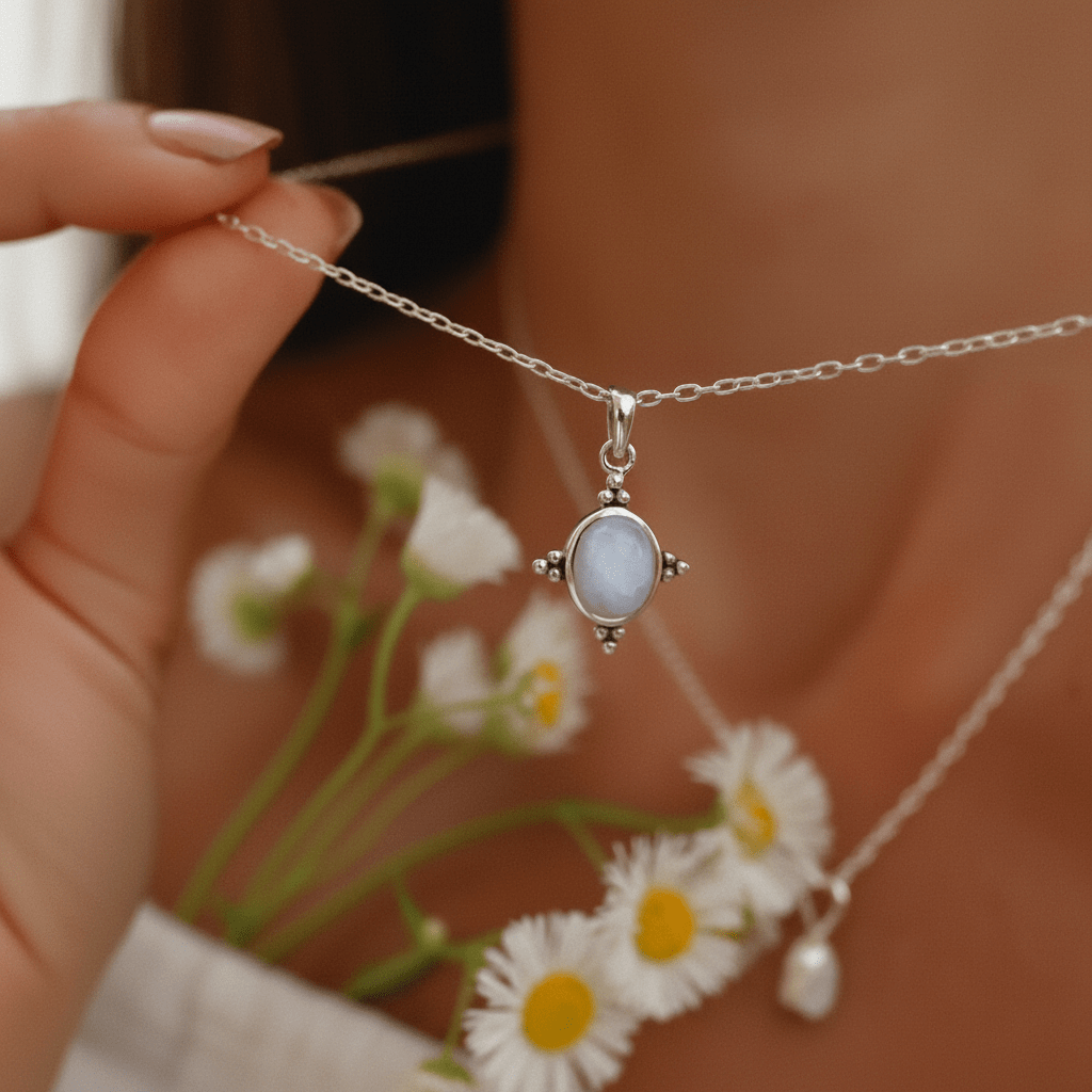 Silver moonstone necklace with a natural moonstone pendant held by a hand, with daisies in the background