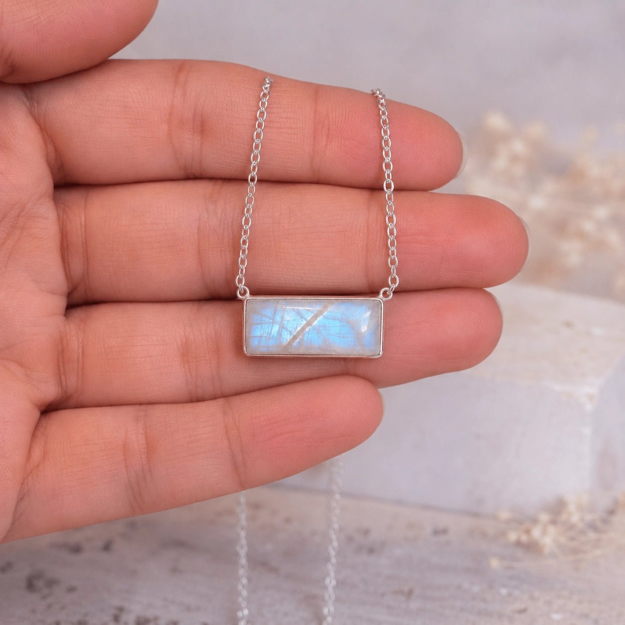 Sterling silver Necklace with a rectangular moonstone pendant held between fingers against a neutral background
