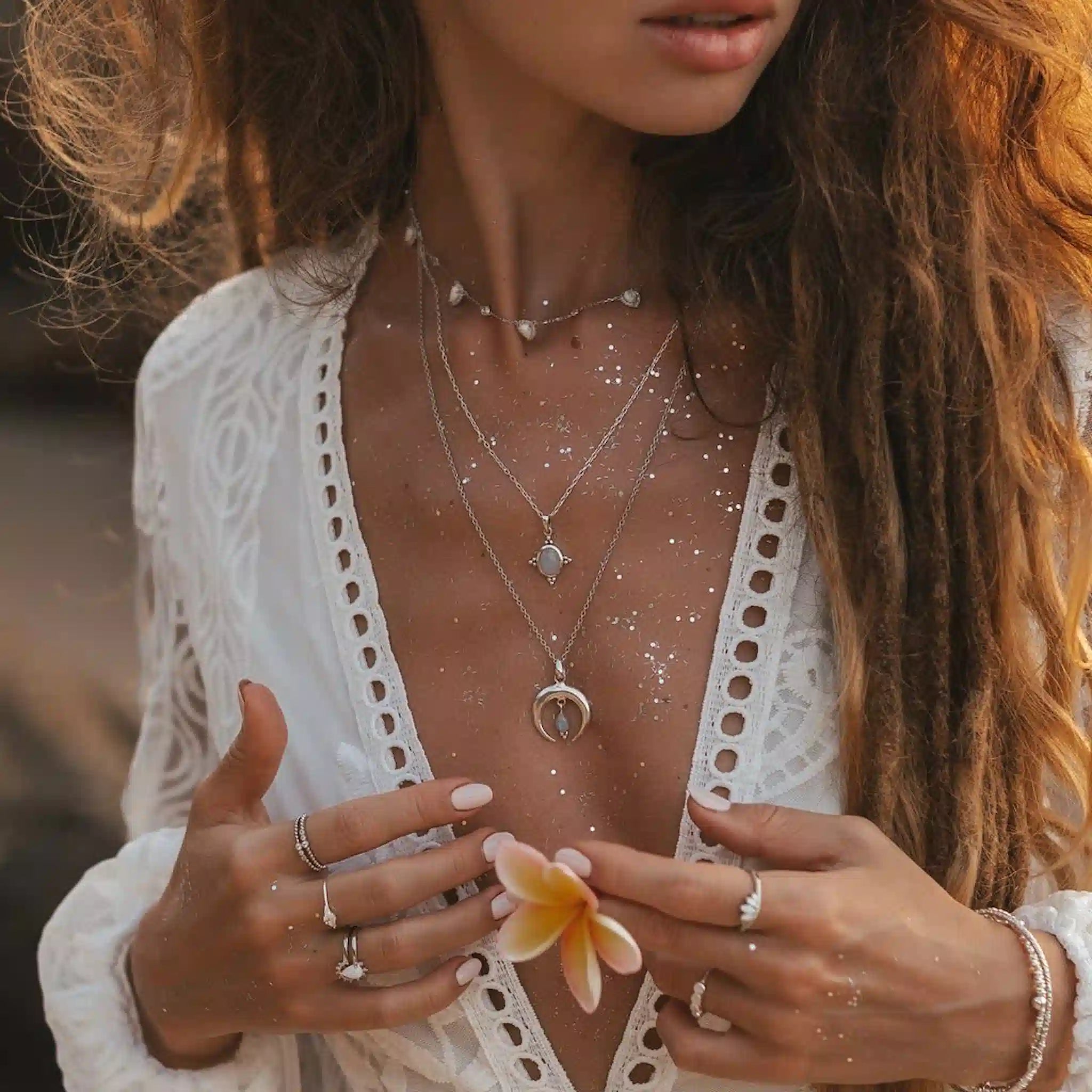 Woman holding a flower with layered sterling silver moonstone necklaces and jewelry in a blurred outdoor setting