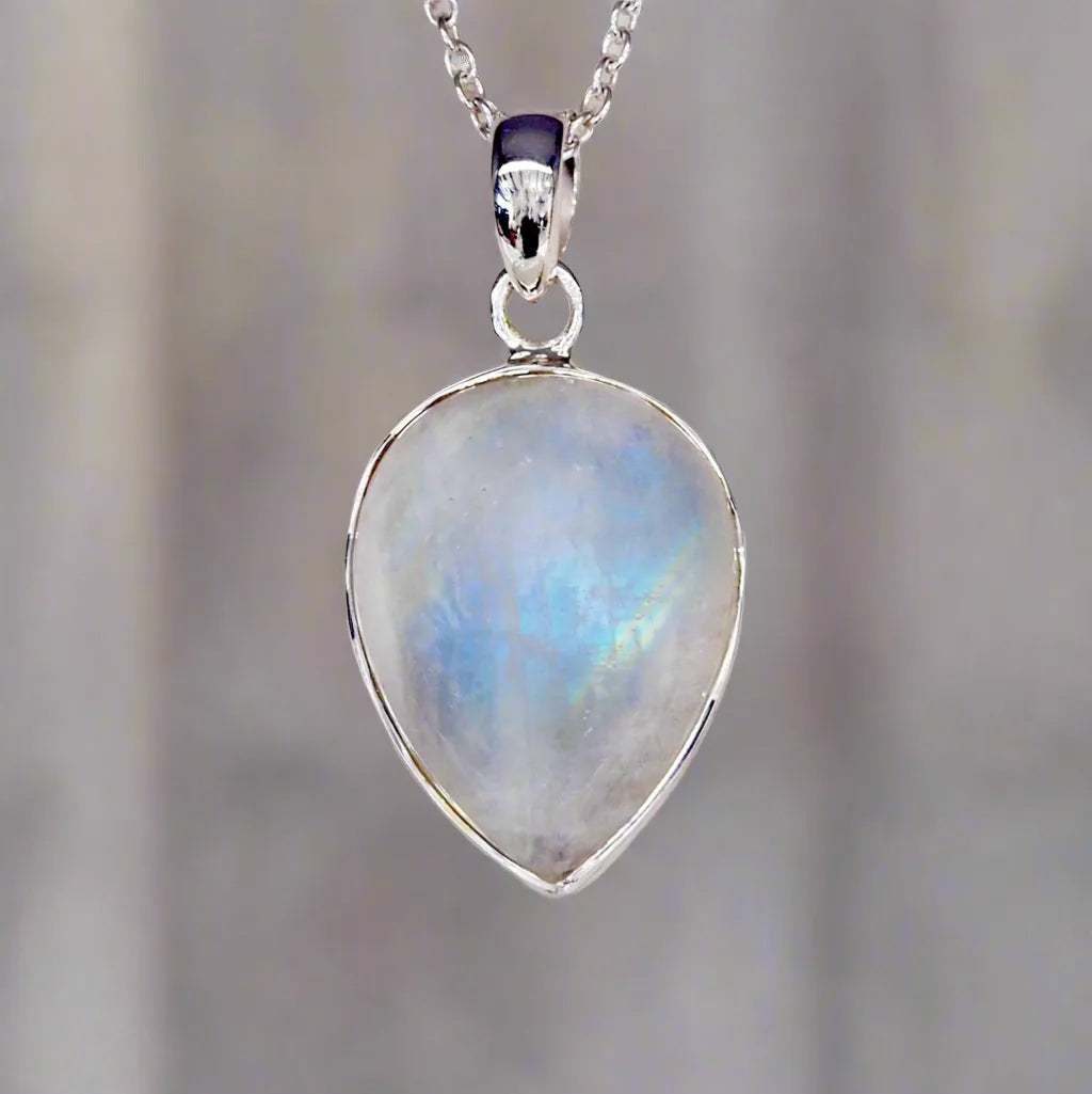 Teardrop-shaped rainbow moonstone pendant on a silver chain against a blurred background