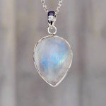 Teardrop-shaped rainbow moonstone pendant on a silver chain against a blurred background
