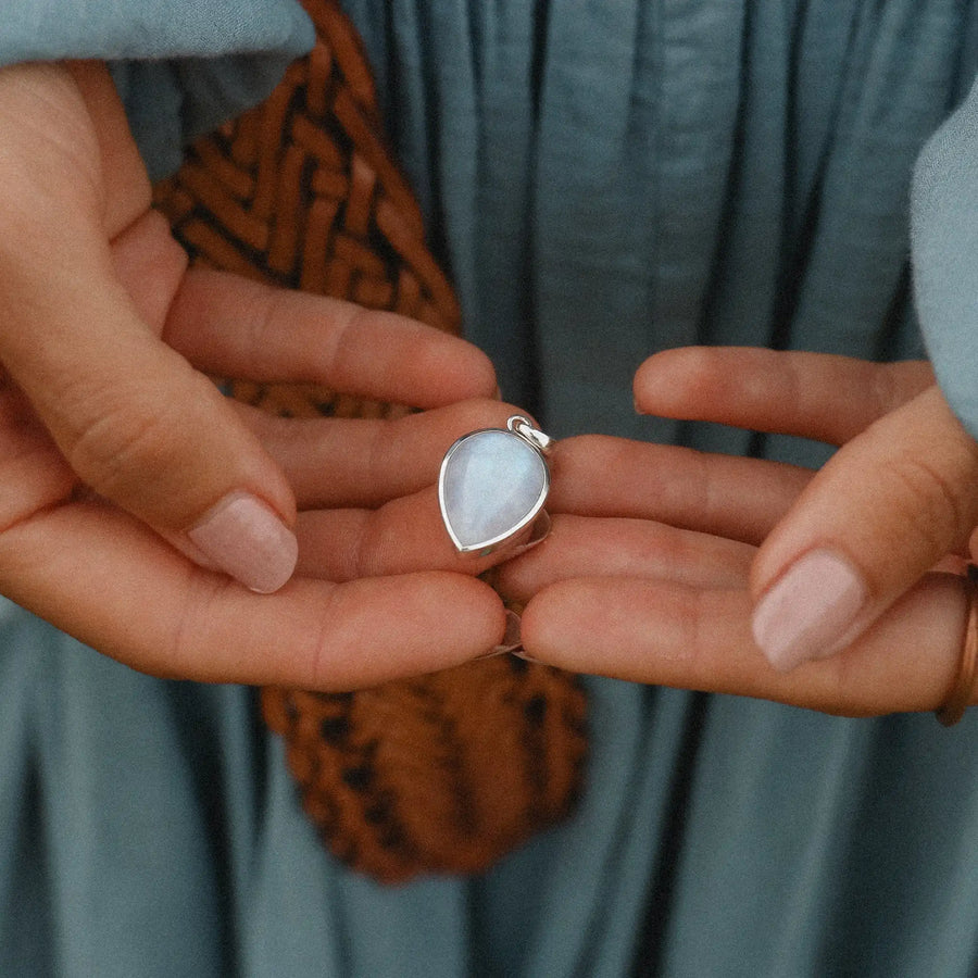 Woman holding teardrop shaped pendant with a rainbow moonstone in it.