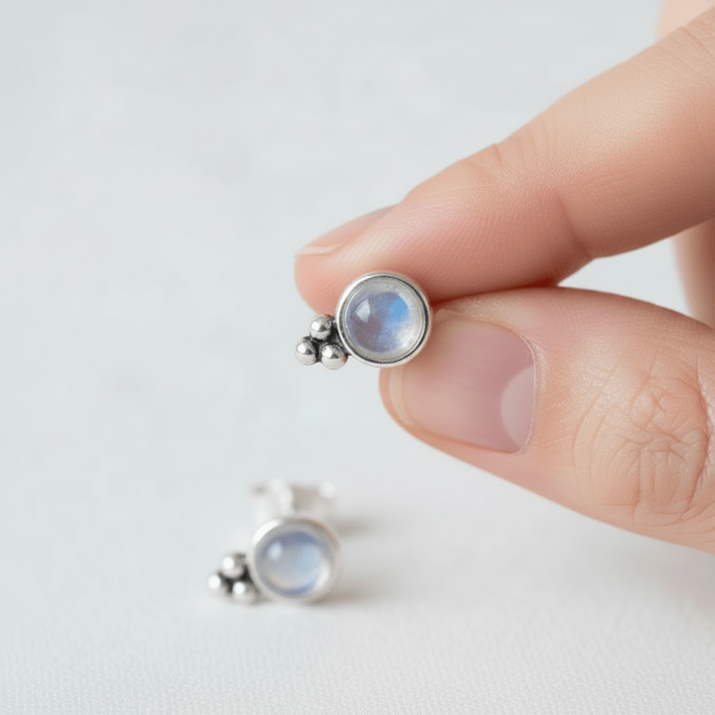 Silver earrings with a gemstone held between fingers on a light background