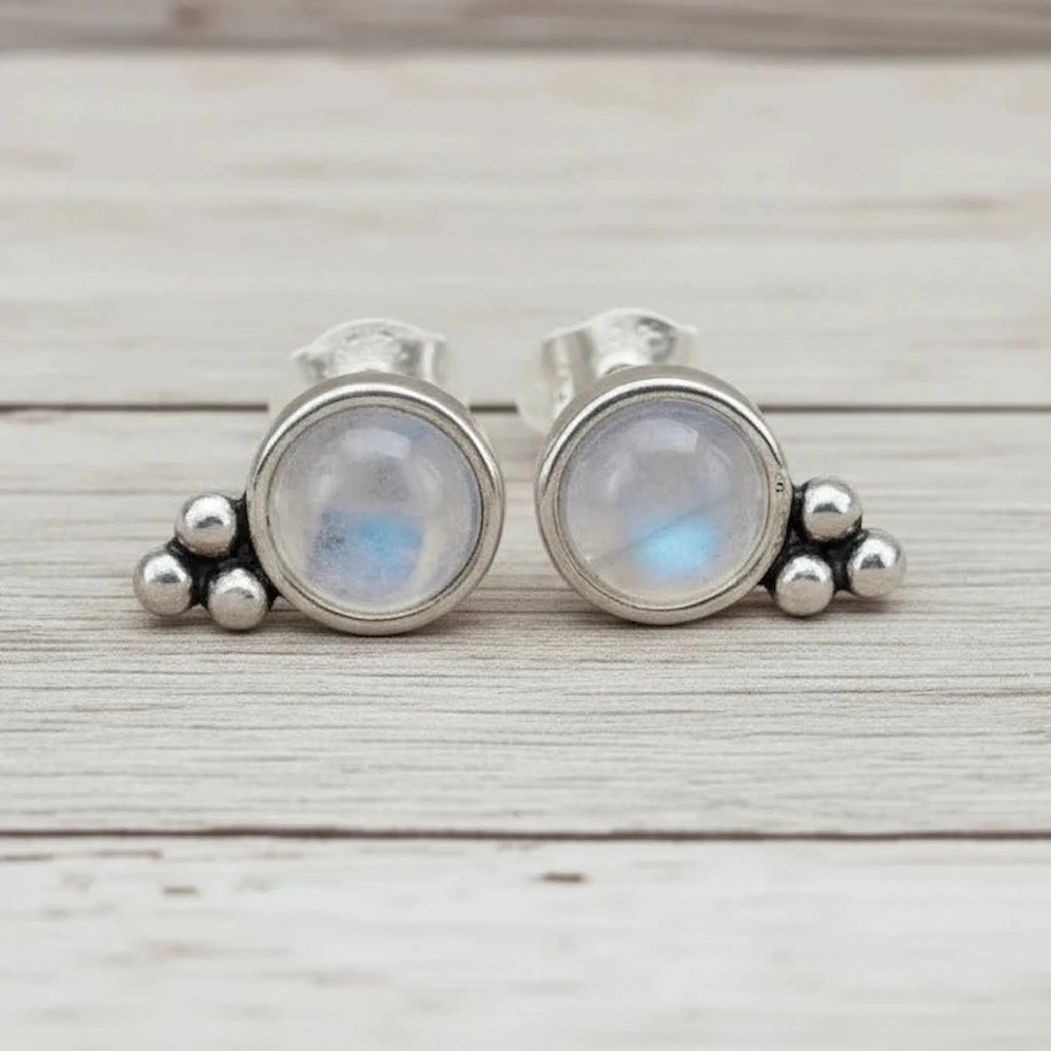Pair of silver earrings with moonstone stones on a wooden surface