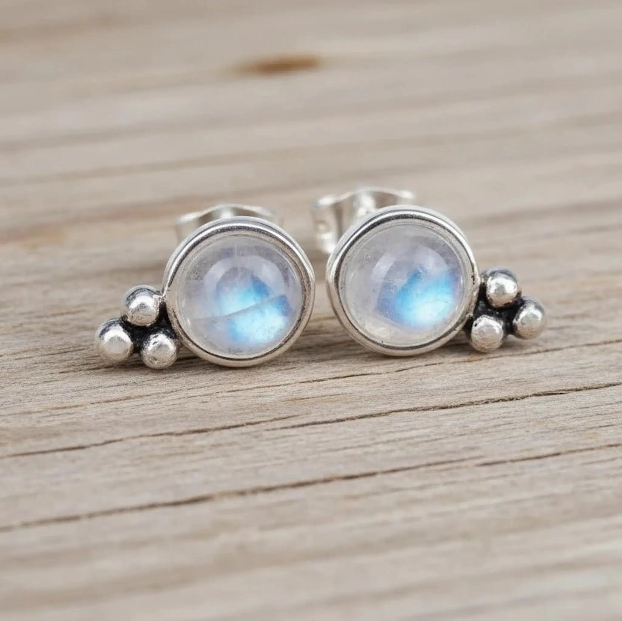 Sterling Silver Stud Earrings with faceted cabochon natural moonstones on a wooden surface