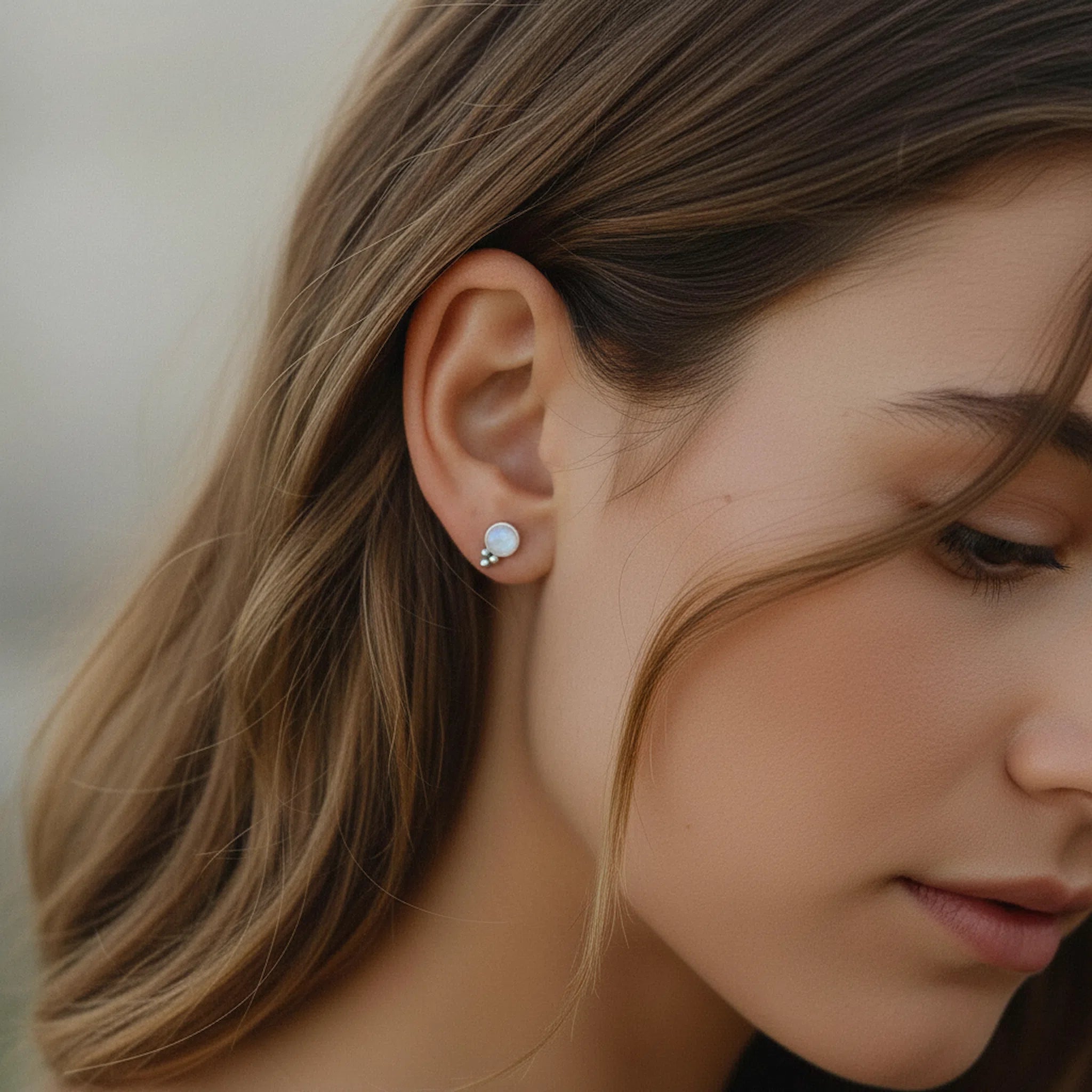 Close-up of a woman wearing a silver earring with a small round moonstone.