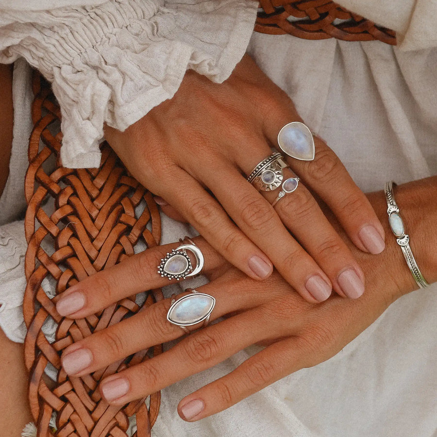 Woman hands crossed on her leg wearing rainbow moonstone rings stacked on both hands.
