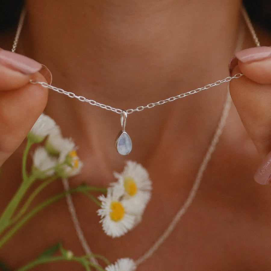 Woman holding up small teardrop shaped rainbow moonstone necklace.