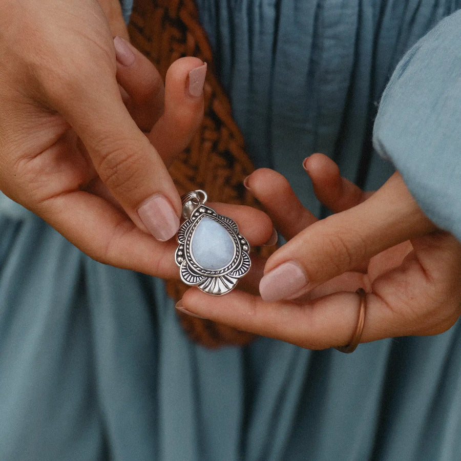 Woman holding rainbow moonstone pendant with flower detailing in the metal surrounding it.