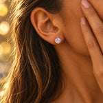Close-up of a woman wearing a round faceted claw-set mystic quartz stud earring