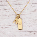 Gold Initial N Pendant and Cancer Zodiac Pendant Necklace on a fine gold chain against a light wooden background