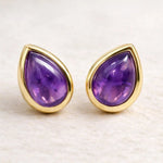 Gold-framed february birthstone teardrop amethyst stud earrings on a light background