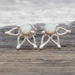 A pair of sterling silver stud earrings featuring round natural australian white opals, displayed on a rustic wooden surface.